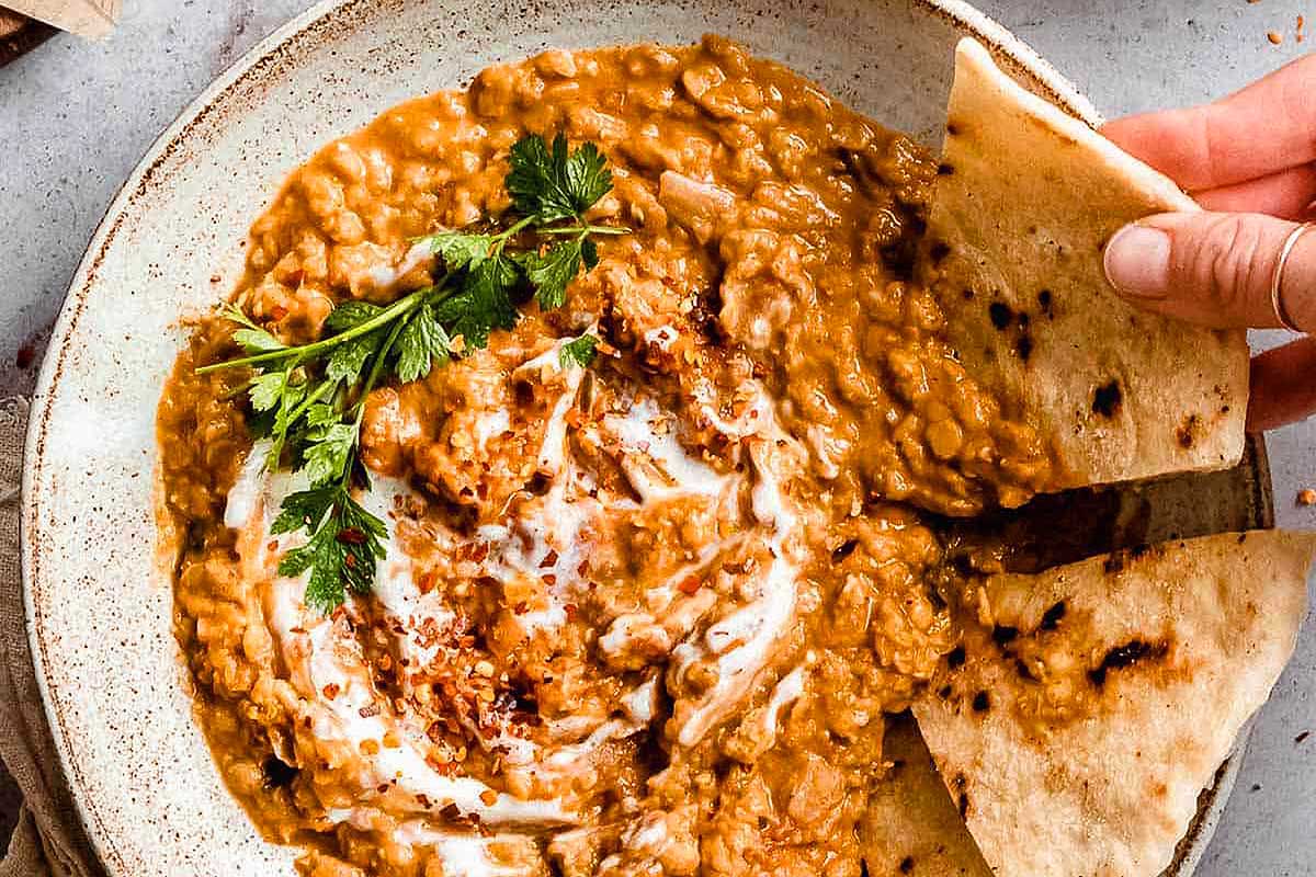 A hand reaching into a bowl of lentil soup.