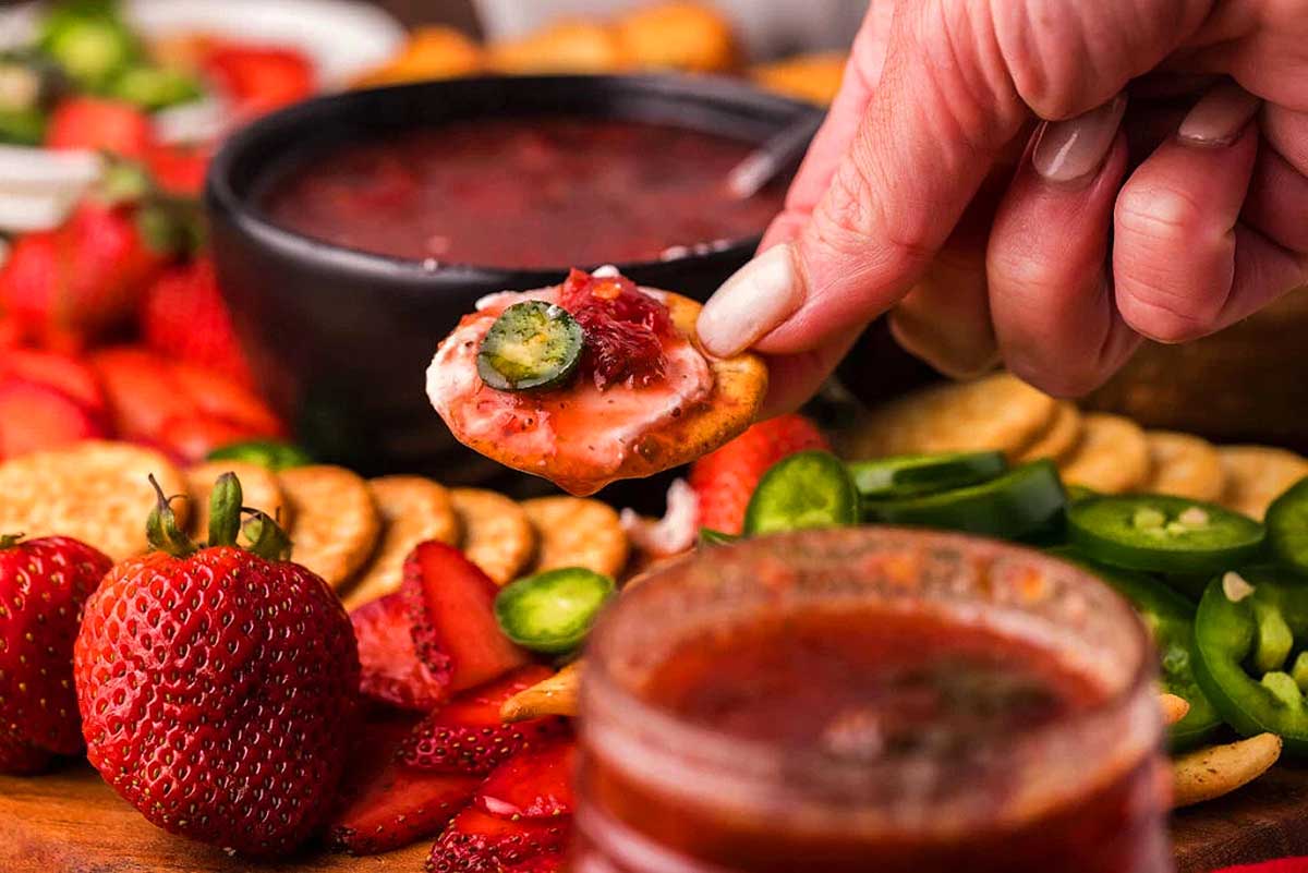 A person dipping a strawberry dip into crackers at a holiday party.