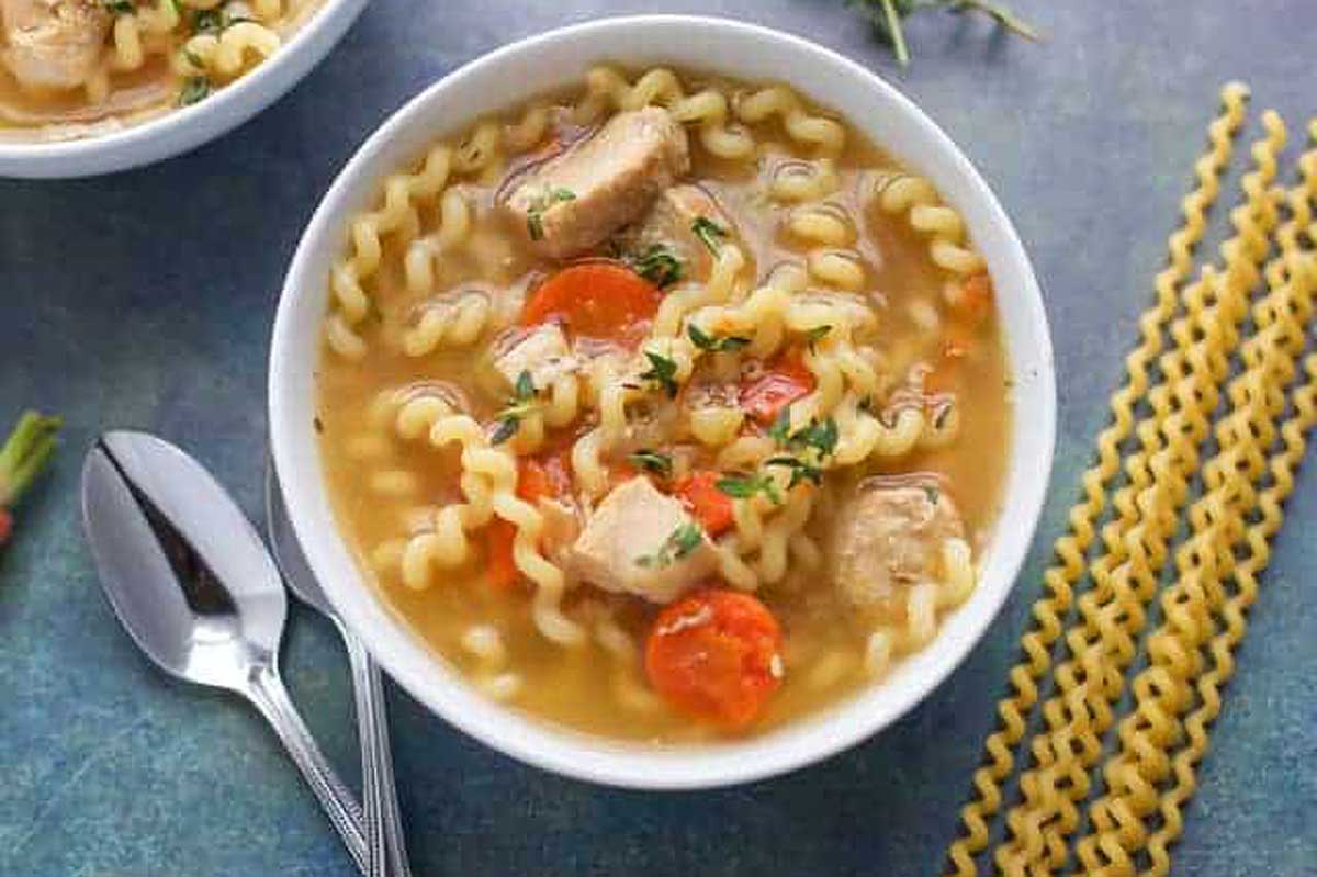 A bowl of chicken noodle soup with noodles and carrots.