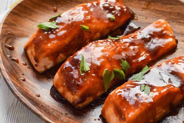 Three salmon fillets with sauce on a wooden plate.