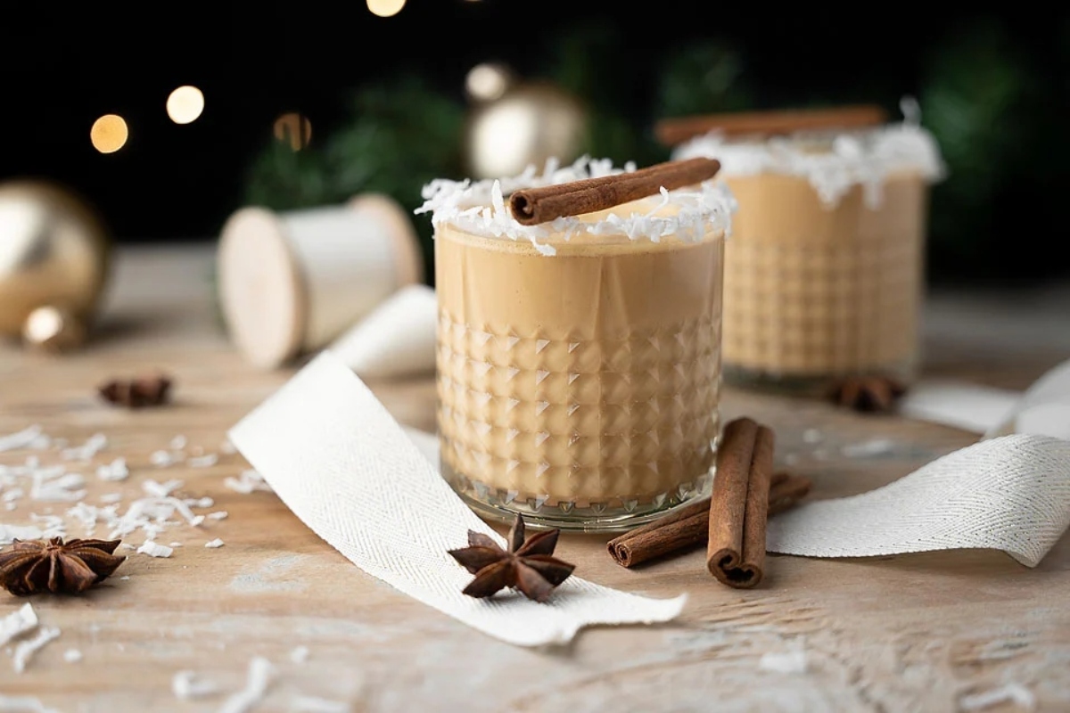 Two glasses of coffee with cinnamon sticks on a wooden table.