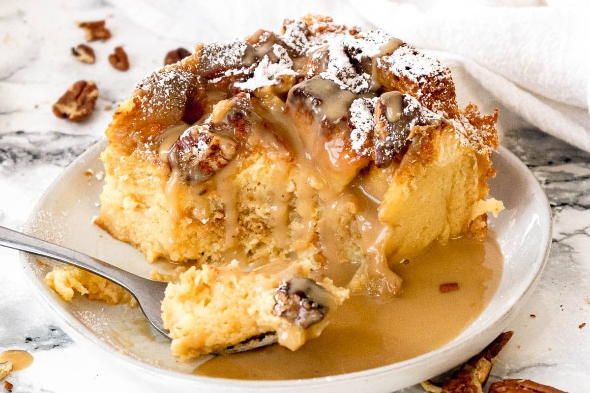 A slice of bread pudding with eggnog caramel sauce and pecans on a plate