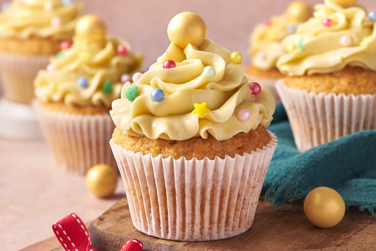 A group of cupcakes with gold icing on a wooden cutting board.