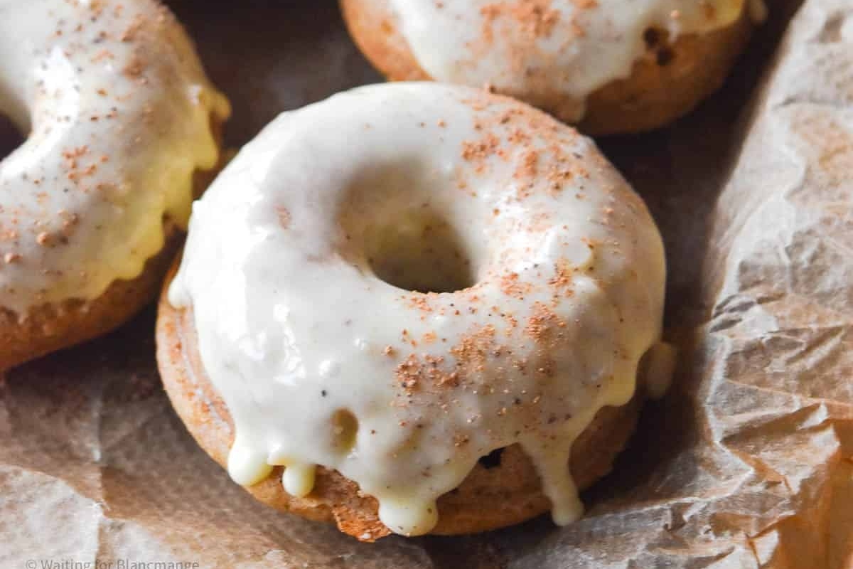 Cinnamon-dusted donuts, coated in a sweet icing, placed delicately on a piece of paper.