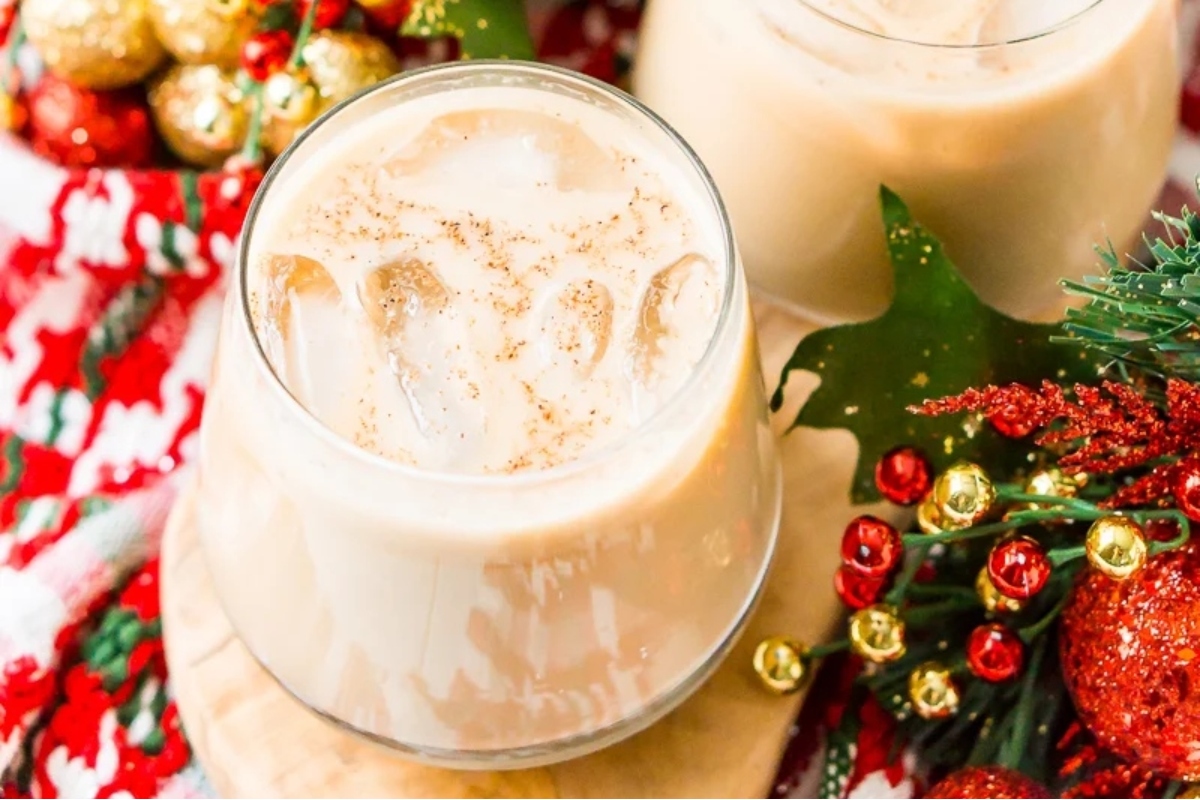 Two glasses of mulled wine and eggnog on a table with Christmas decorations.