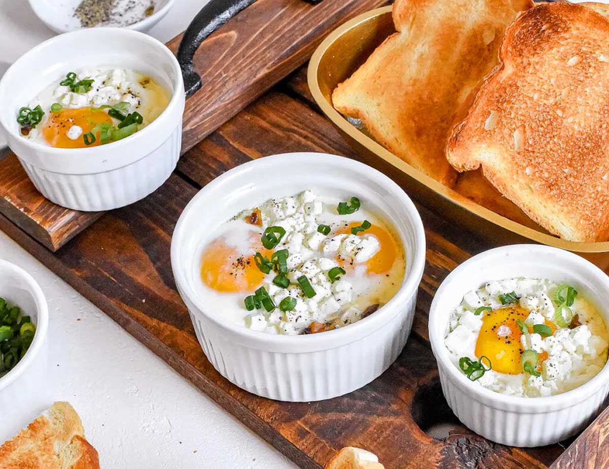 Four bowls of eggs and bread on a wooden cutting board, perfect for brunch recipes.