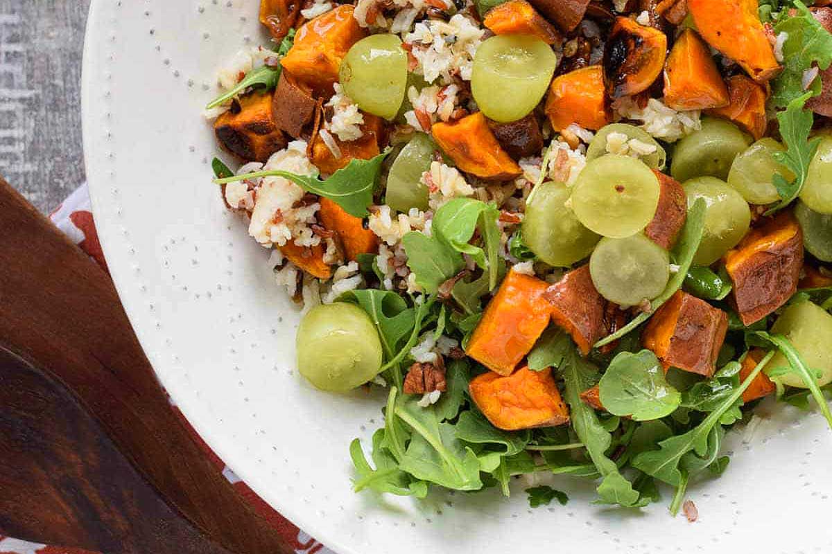 Sweet potato salad with grapes and grapes in a white bowl.