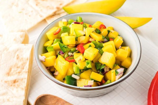 Mango salsa in a bowl next to a wooden spoon.