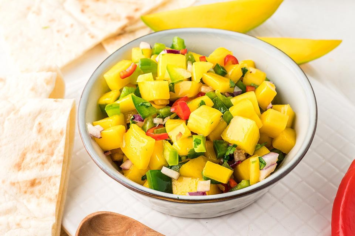 Mango salsa in a bowl next to a wooden spoon.