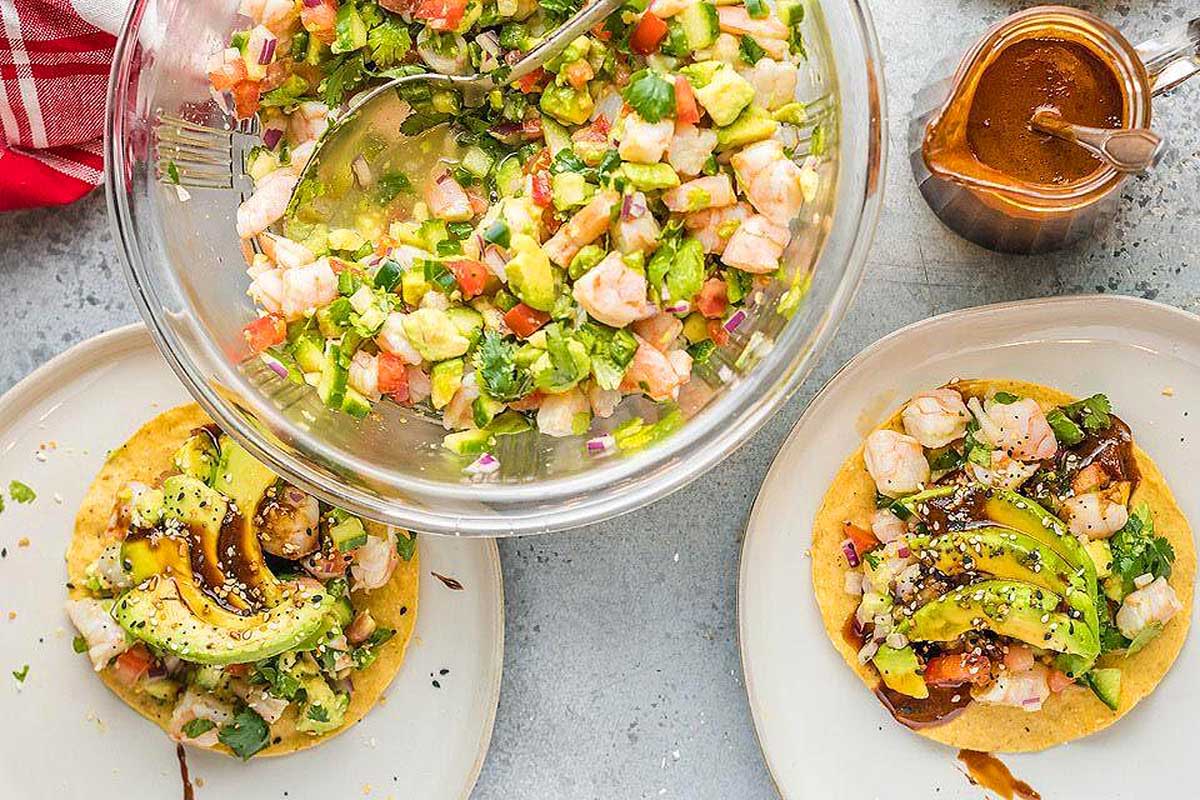 Two plates of shrimp and avocado tacos with a bowl of salsa.