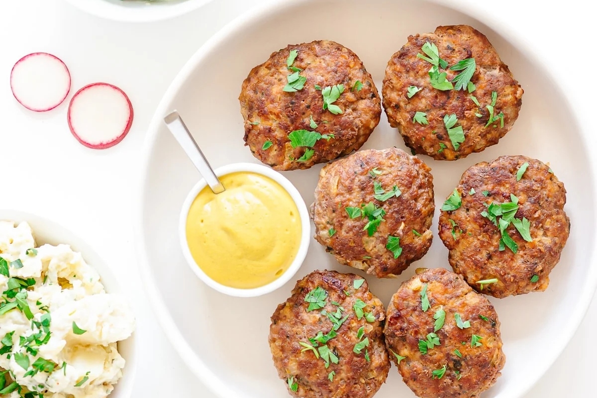 A plate of German meatballs served with a bowl of dipping sauce.
