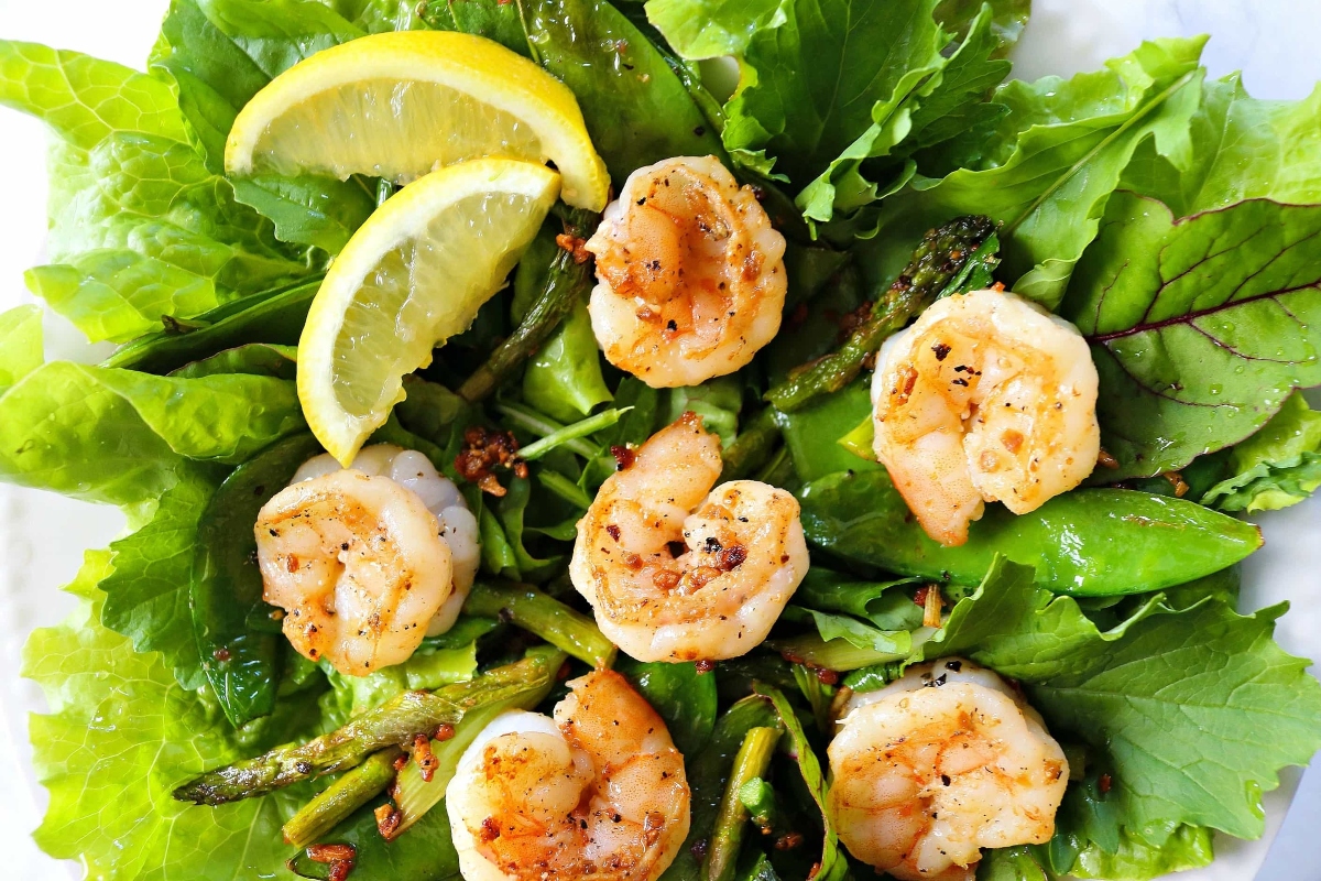 Grilled shrimp salad on a white plate with lemon wedges.