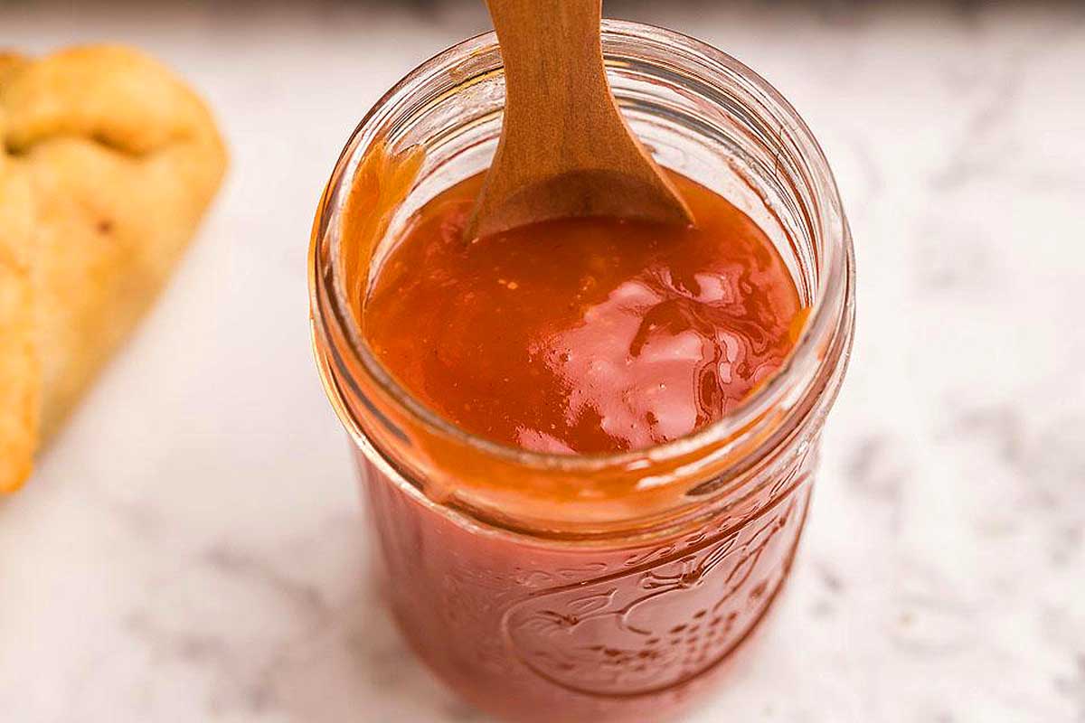 A jar of tomato sauce beside a wooden spoon, perfect for making delicious sauce recipes.