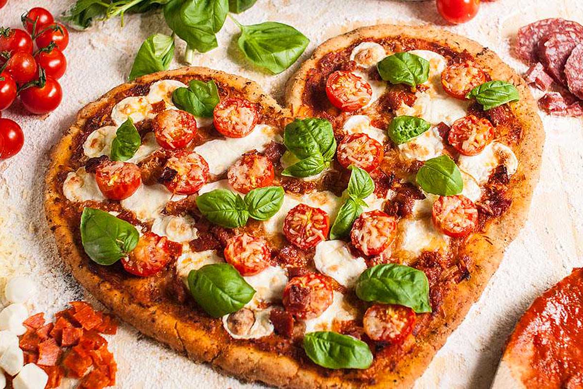 A heart shaped pizza with tomatoes and basil.