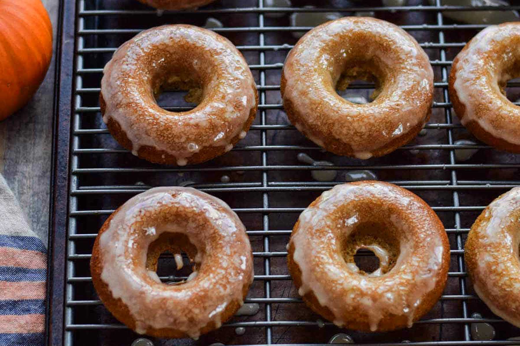 Glazed pumpkin donuts on a cooling rack.