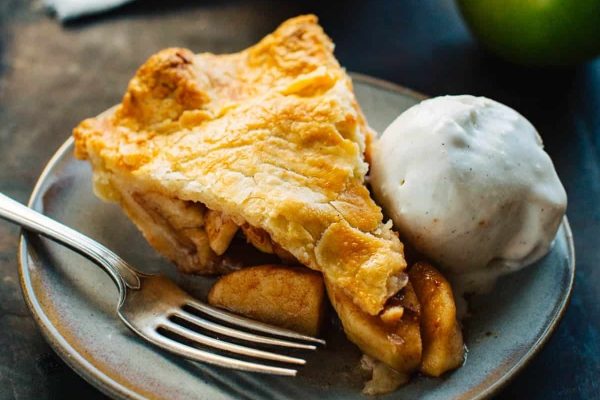 A slice of apple pie on a plate with ice cream, perfect for Thanksgiving.