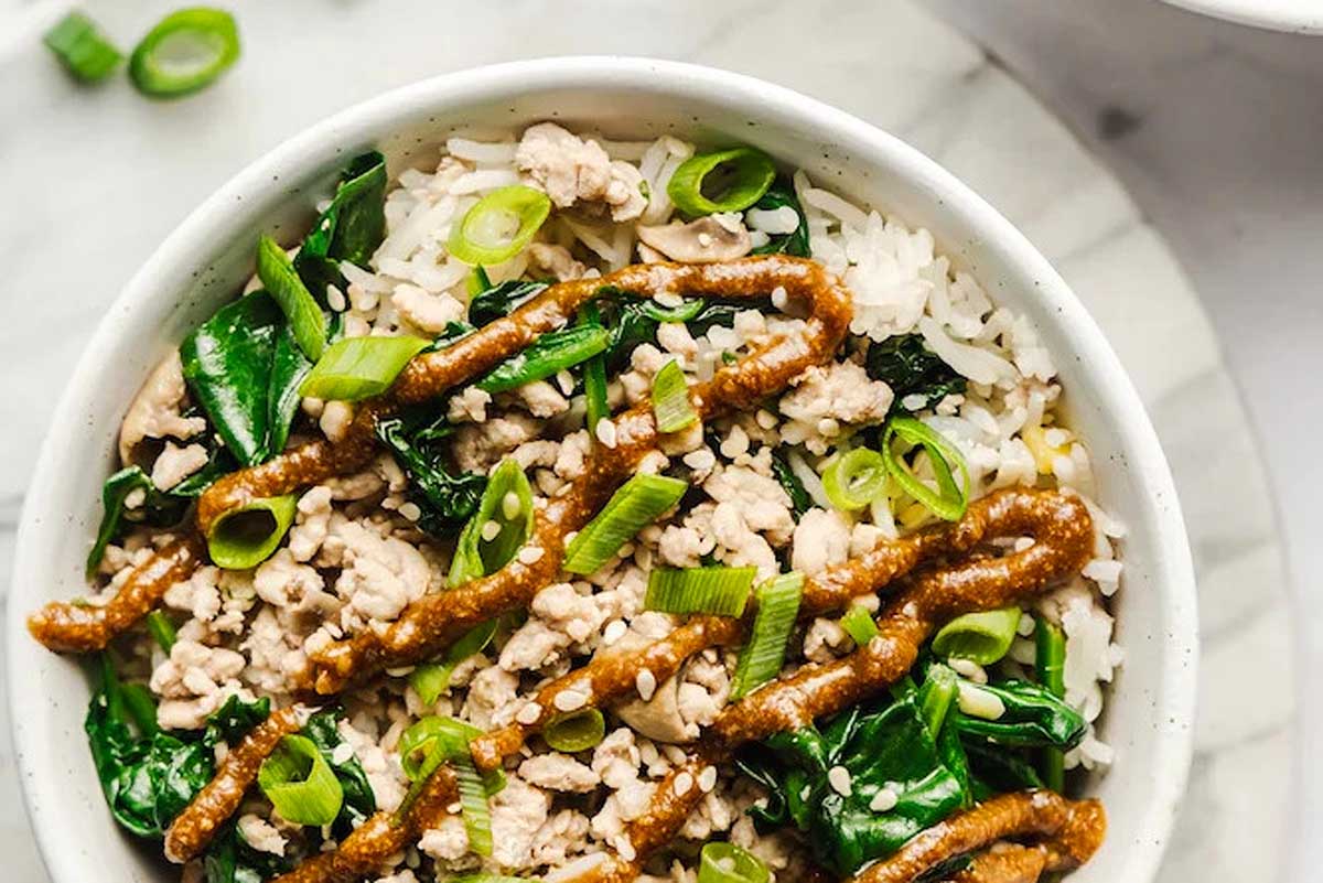 A bowl of rice with meat and greens.