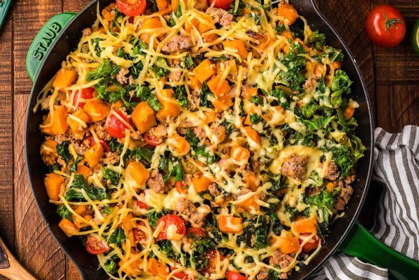 A skillet full of vegetables, meat and cheese.