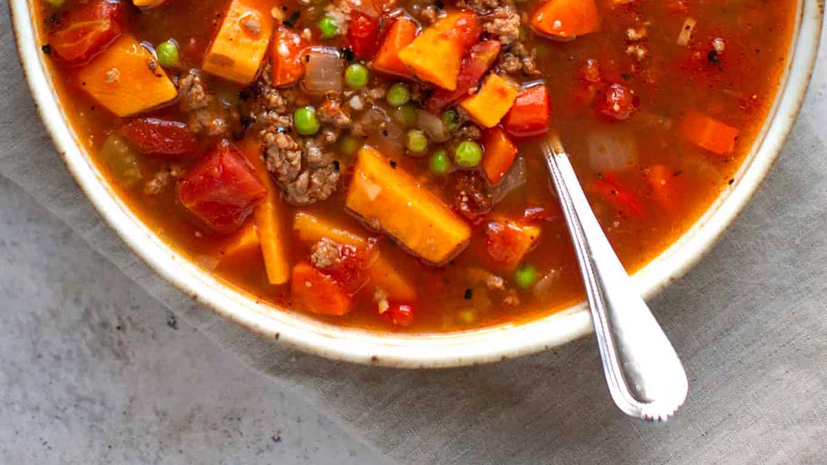 A bowl of soup with meat, vegetables and peas.