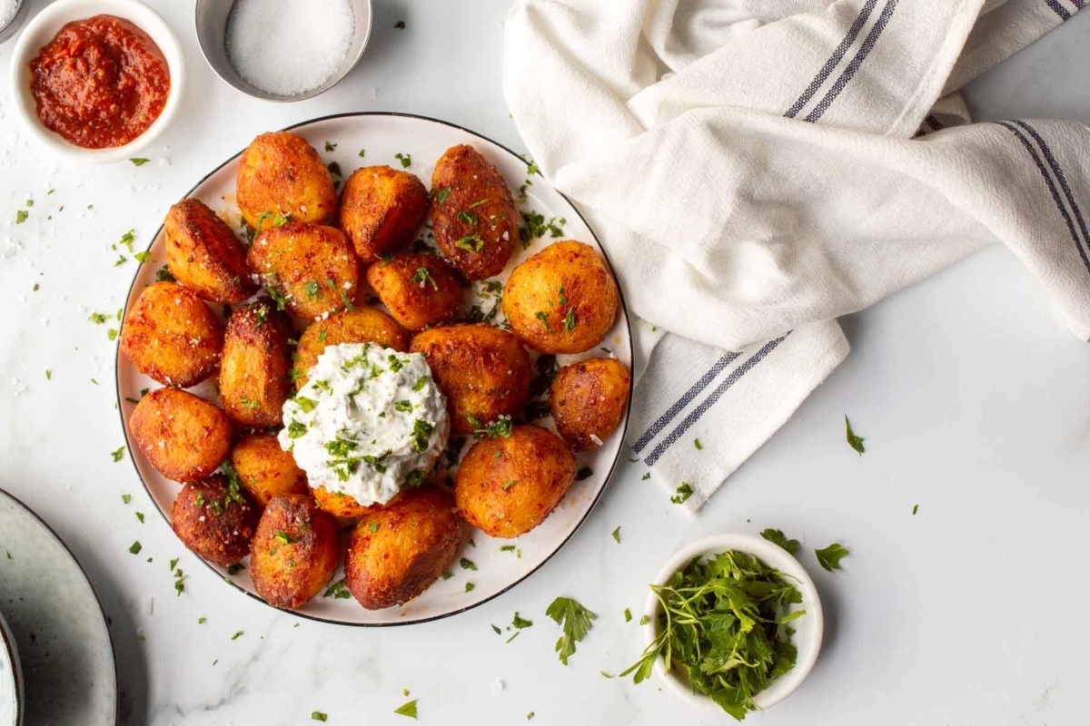 A plate of fried potatoes with sour cream on it.