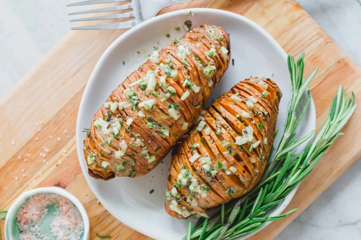 Two grilled sweet potatoes on a plate with sprigs of rosemary.