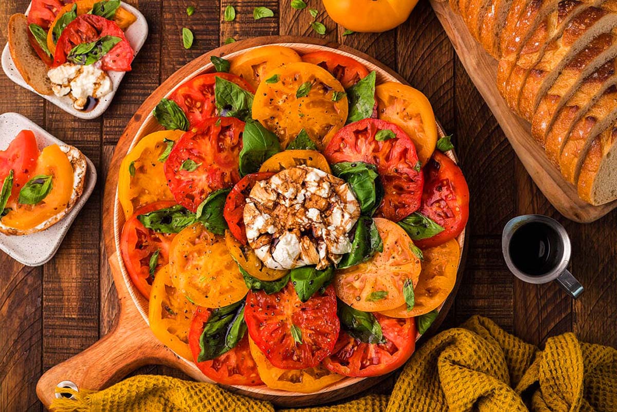 An Italian salad featuring a plate of tomatoes, bread and cheese on a rustic wooden table.