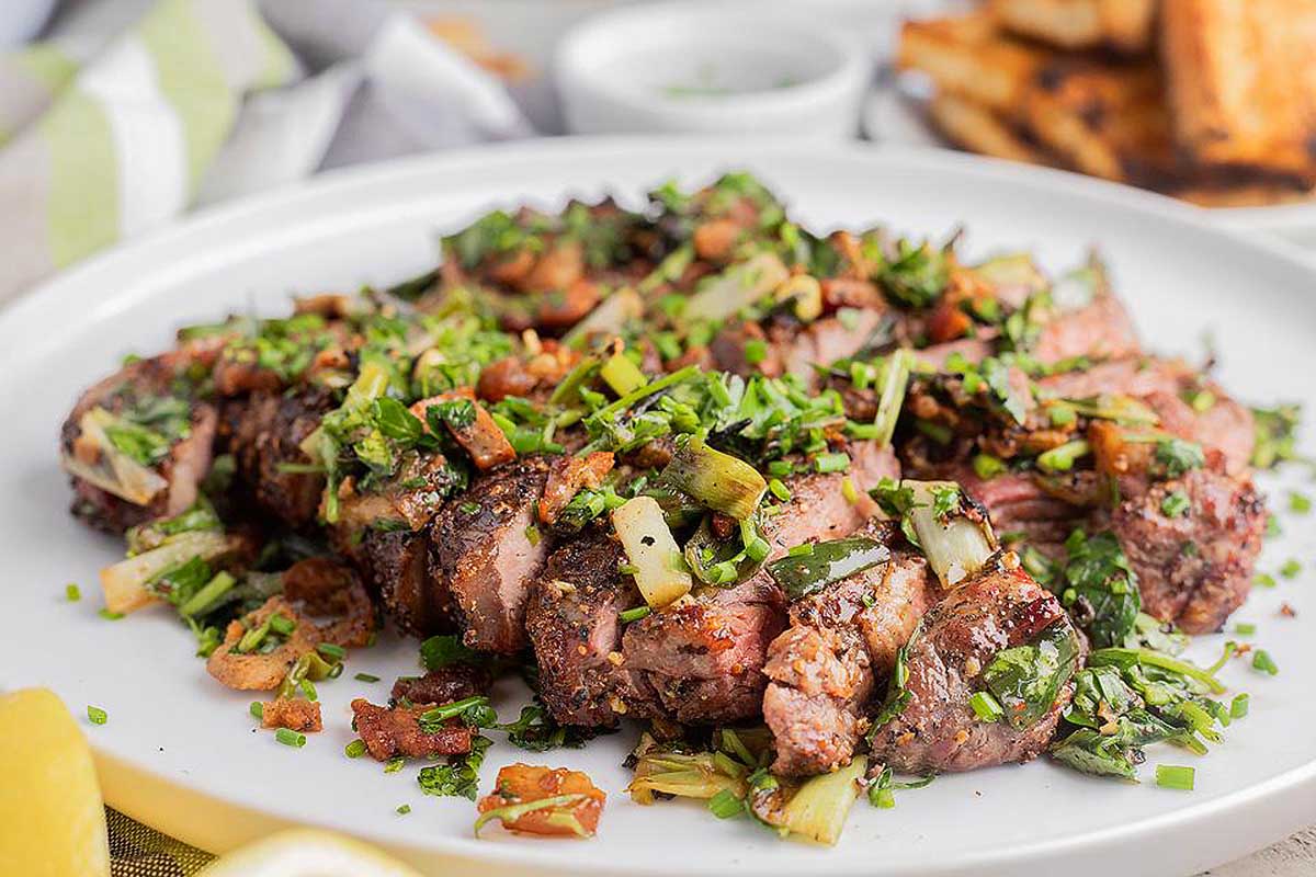 Grilled steak on a white plate with lemon wedges. This is one of the best steak recipes.