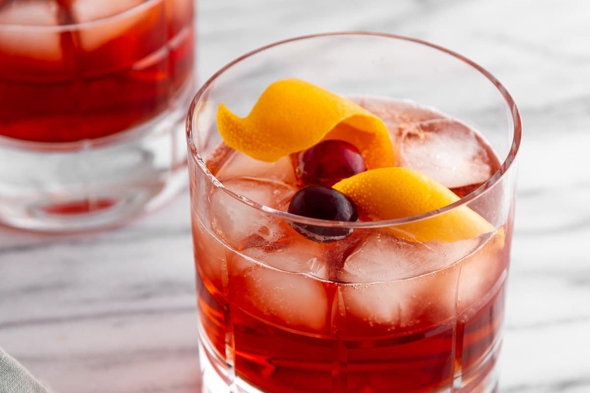 Holiday negroni cocktail in a tumbler glass with orange peel and cranberry garnish.