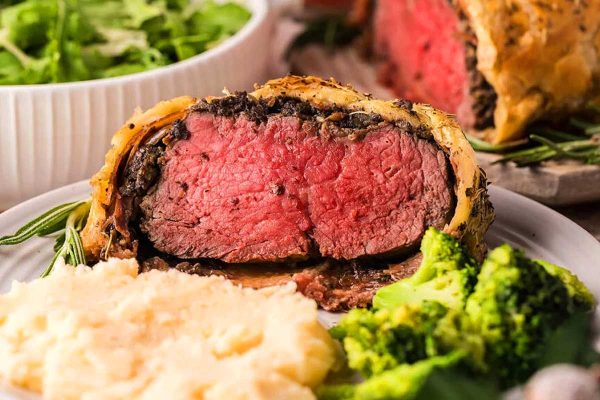 Beef wellington on a wooden board with rosemary sprigs.