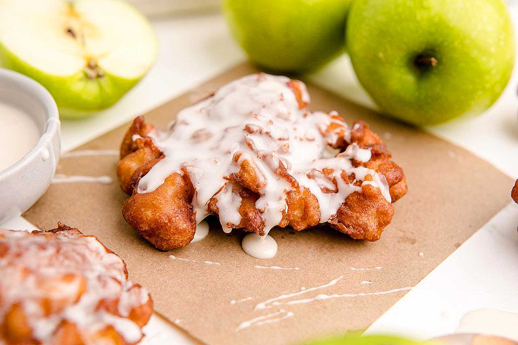 A plate of apple doughnuts with icing and apples.