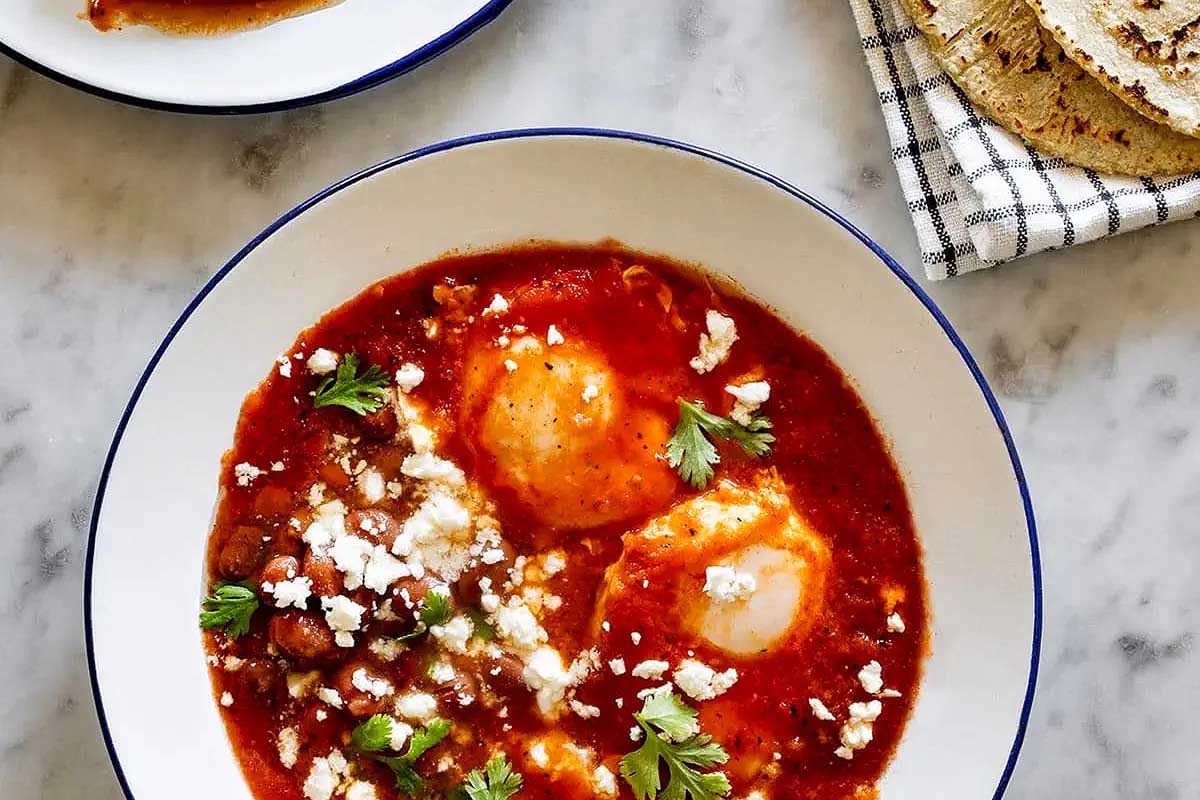 Two bowls of mexican eggs and tortillas on a marble table.
