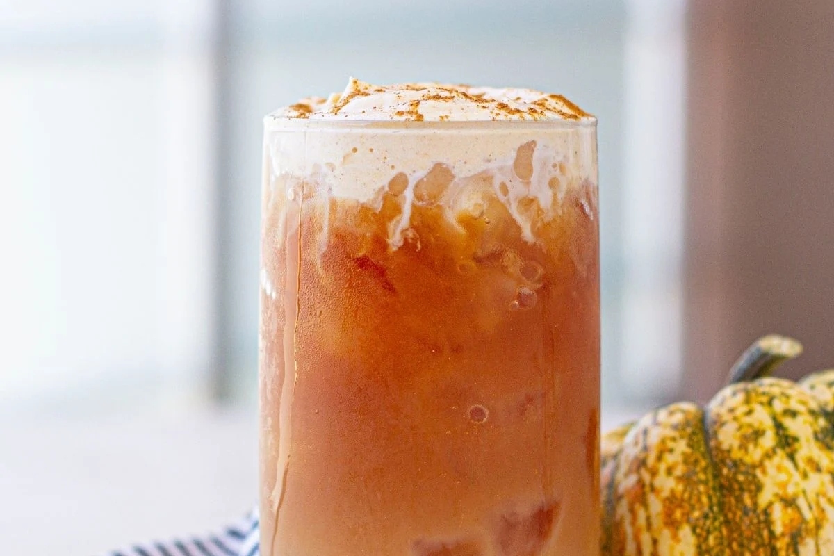 A Starbucks pumpkin spice latte on a table next to pumpkins.