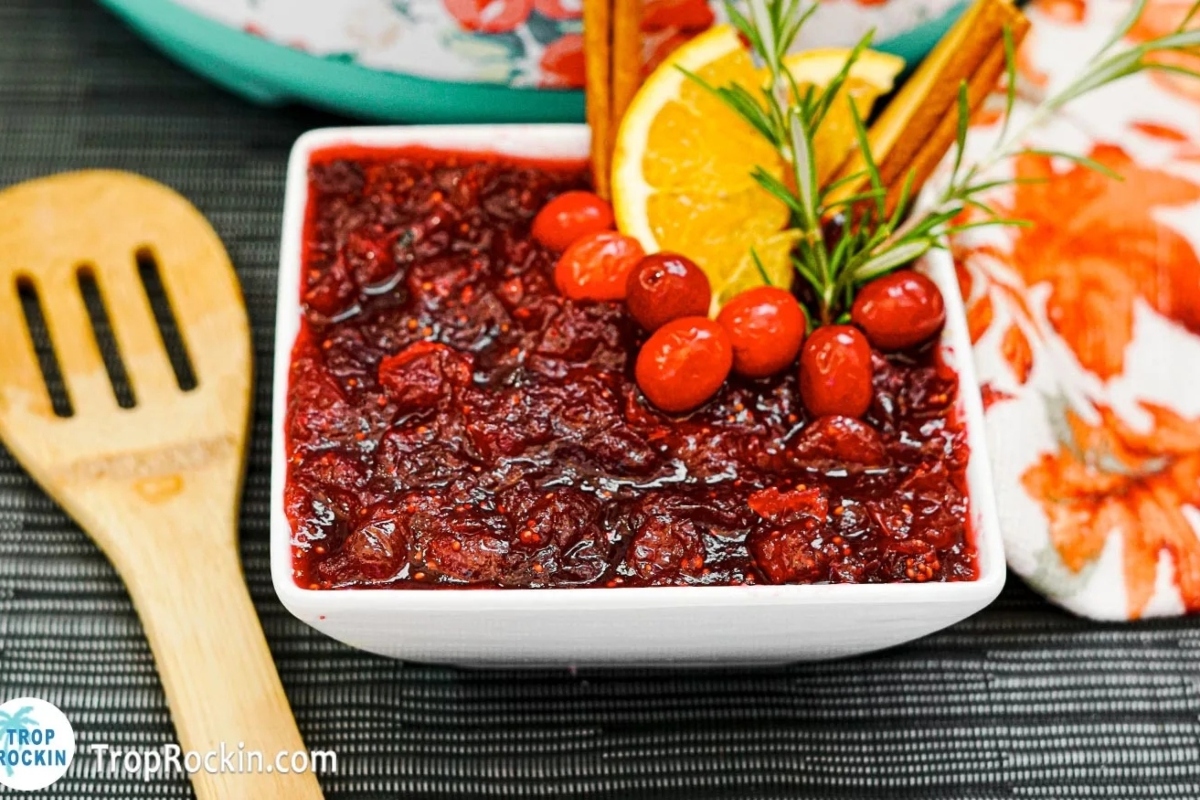 Cranberry sauce recipes in a white bowl with oranges and cinnamon sticks.