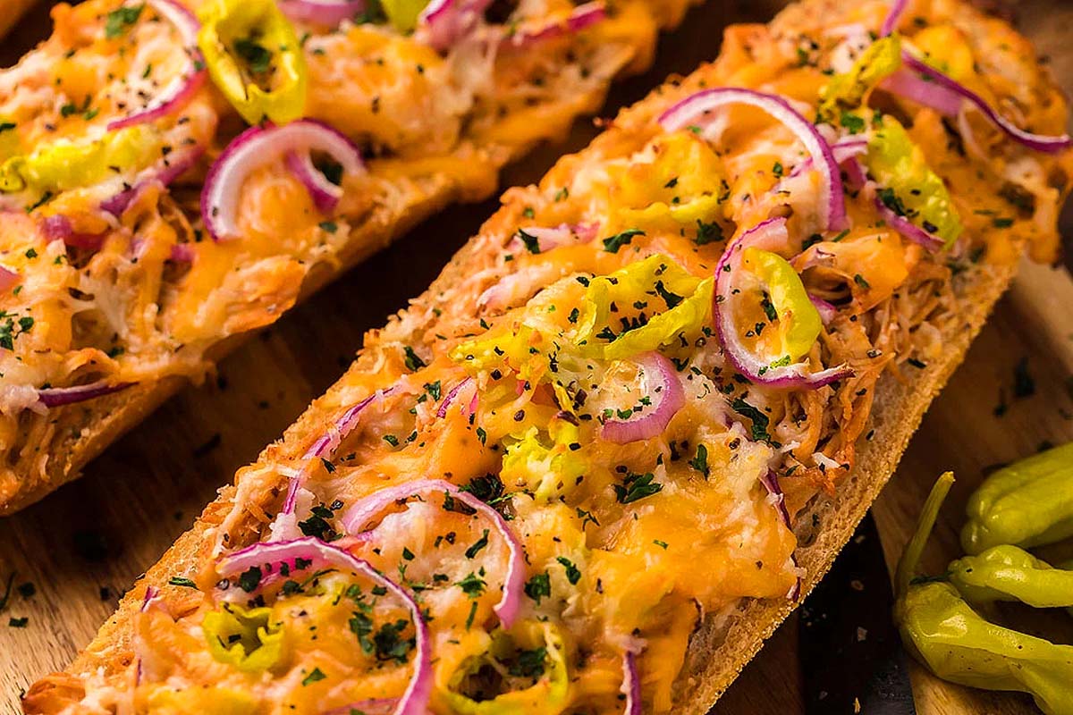 Two breads with onions and peppers on a cutting board.