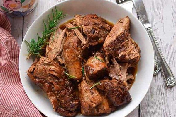 A bowl of pulled pork with rosemary sprigs and a fork, perfect for an Instant Pot Thanksgiving.