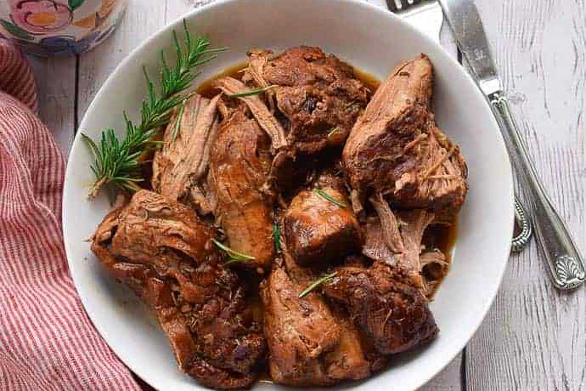 A bowl of pulled pork with rosemary sprigs and a fork, perfect for an Instant Pot Thanksgiving.