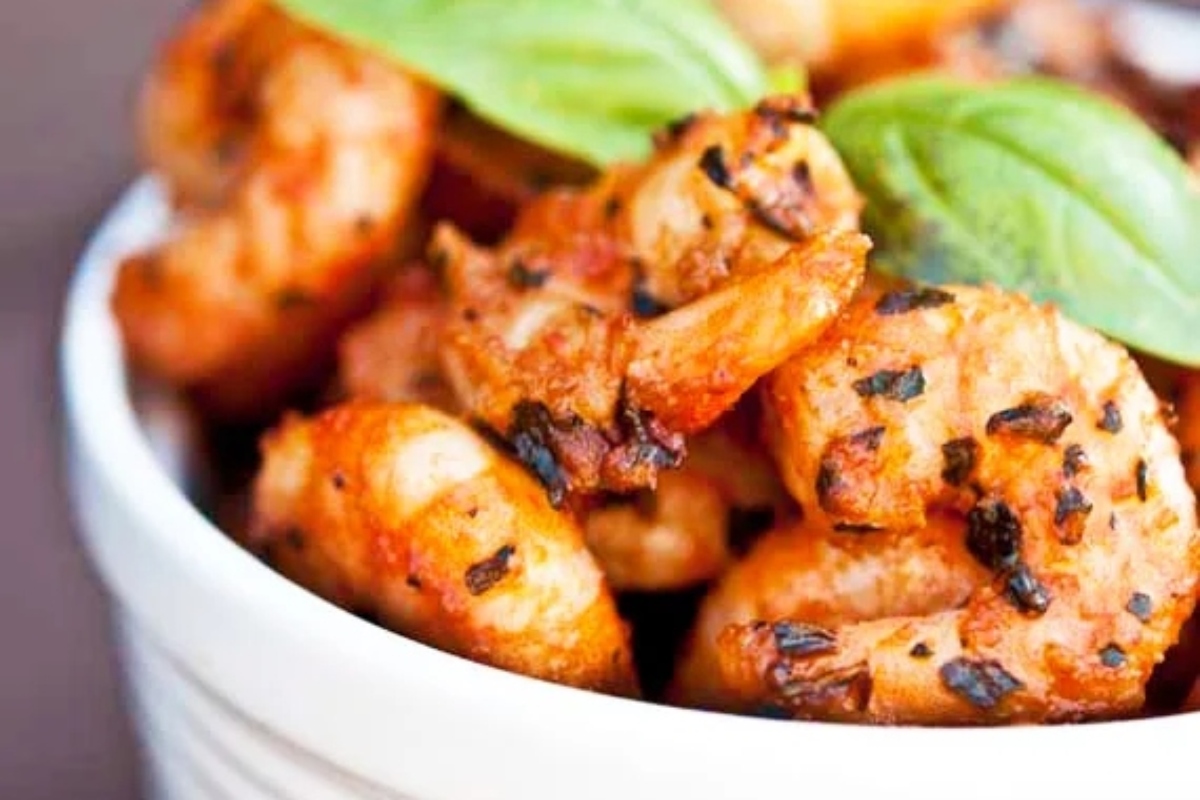 Grilled shrimp in a white bowl with basil leaves.