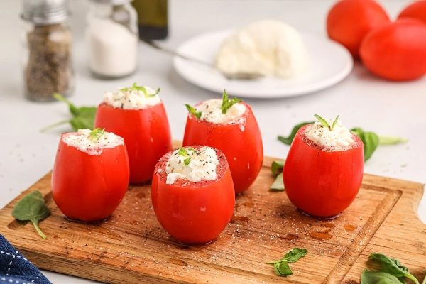Stuffed tomatoes with feta cheese on a wooden cutting board.