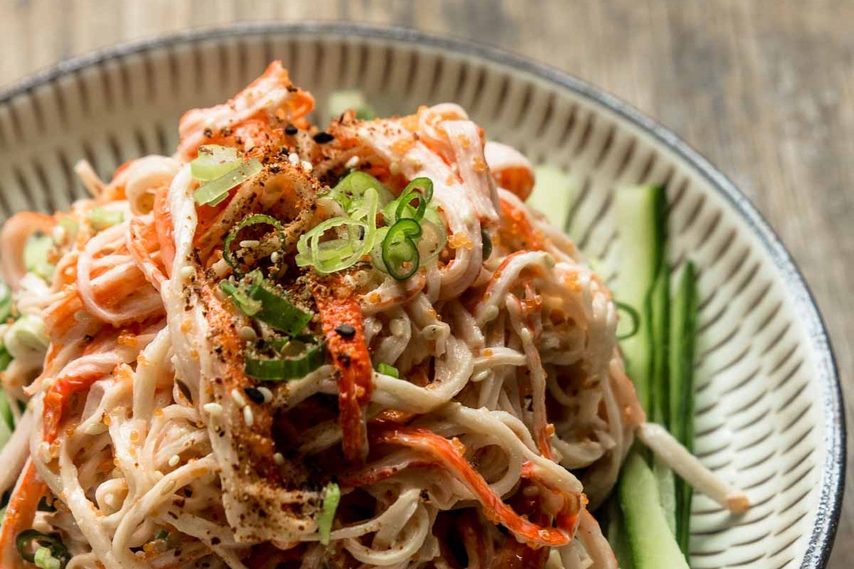 A bowl of noodles with carrots and cucumbers.