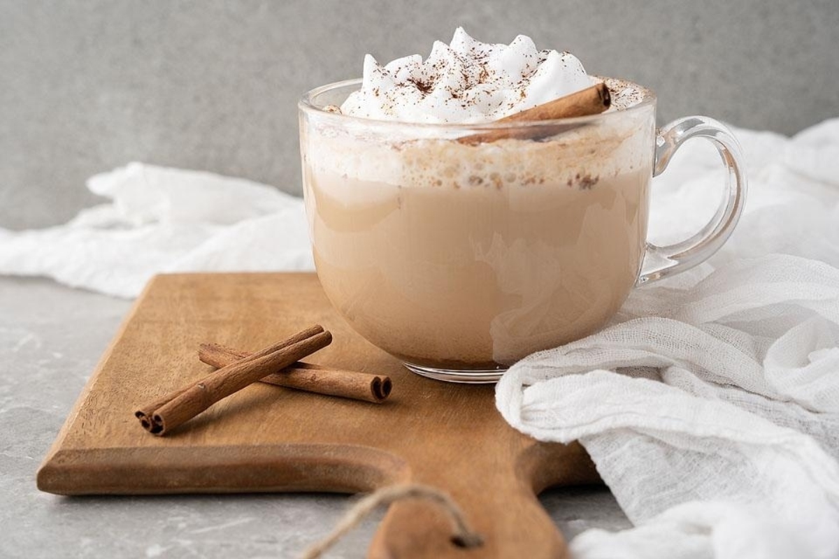 A festive Starbucks latte adorned with cinnamon and whipped cream, elegantly presented on a rustic wooden cutting board for the ultimate holiday recipe indulgence.