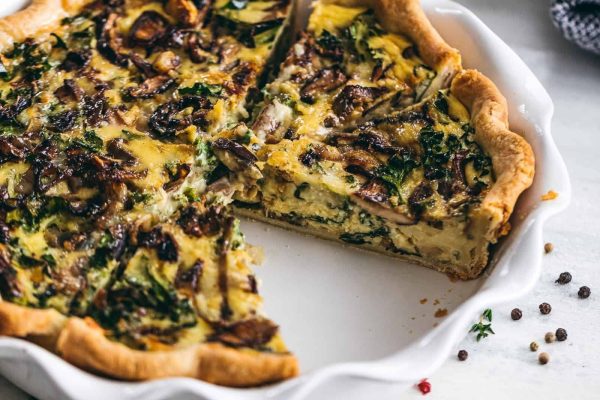 A delicious quiche recipe featuring spinach and mushrooms, elegantly plated on a white dish.