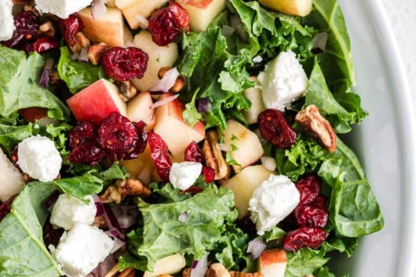 A bowl of kale salad with apples and cranberries.