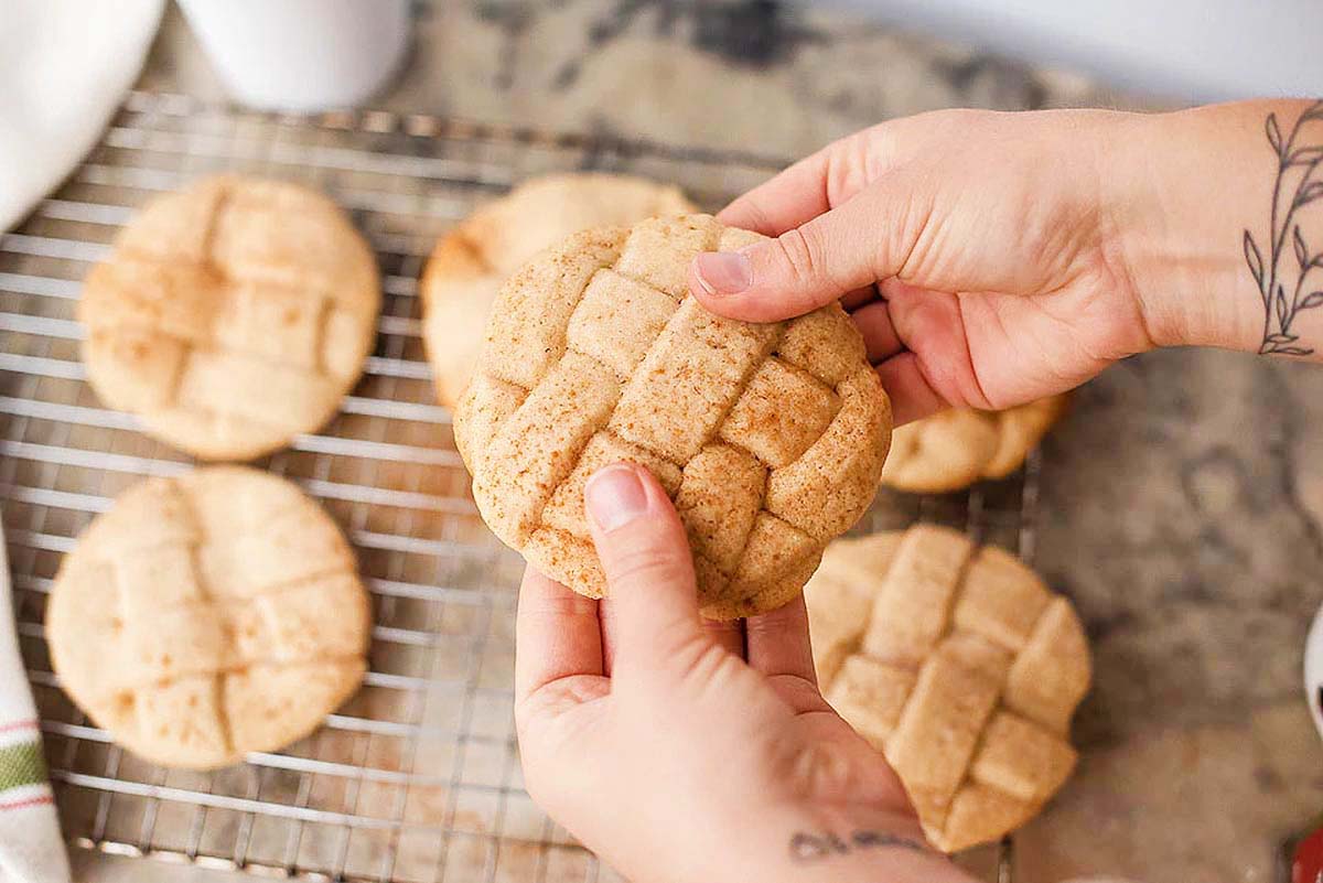 A person holding a cinnamon cookie on a cooling rack.