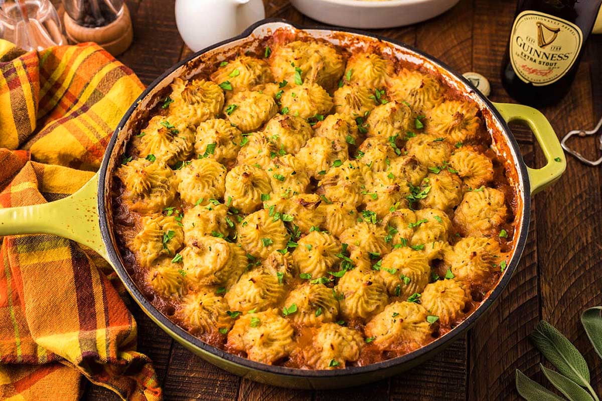 A skillet full of mashed potatoes on a table at a pub, next to a bottle of beer.