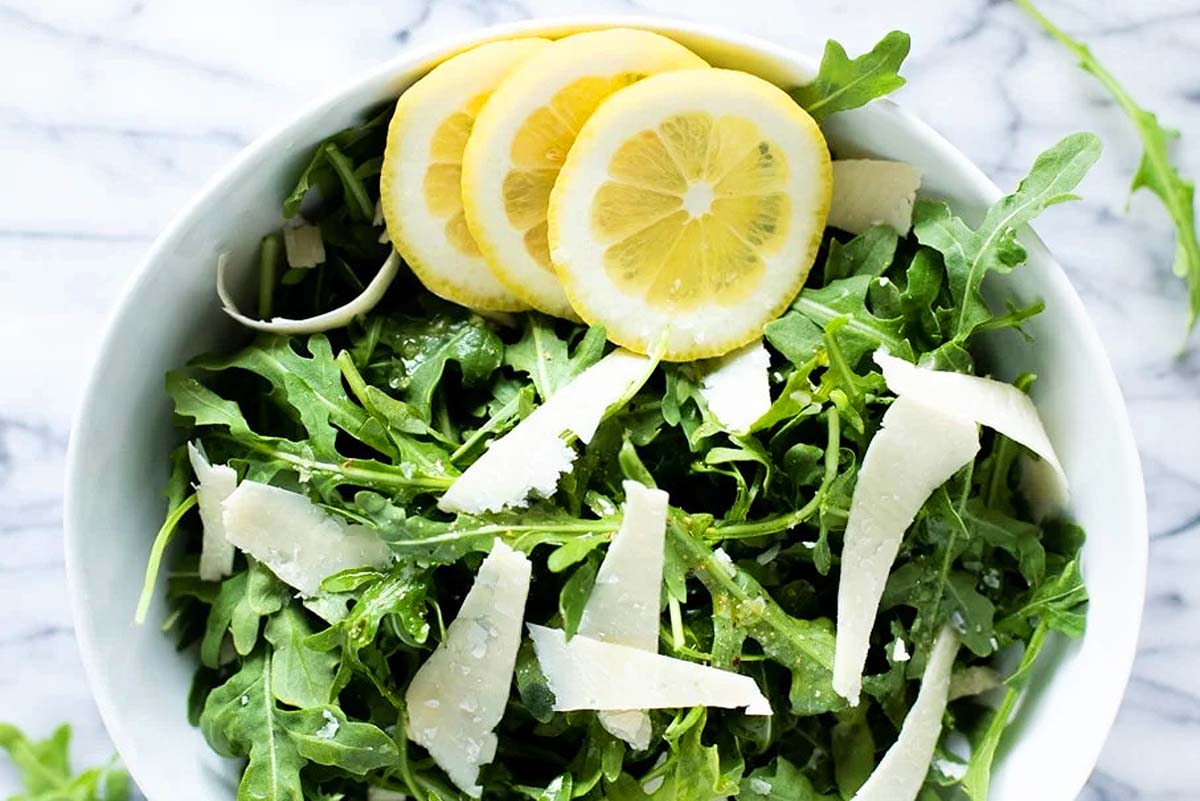 An Italian salad recipe featuring a bowl of arugula salad with lemon slices and parmesan.