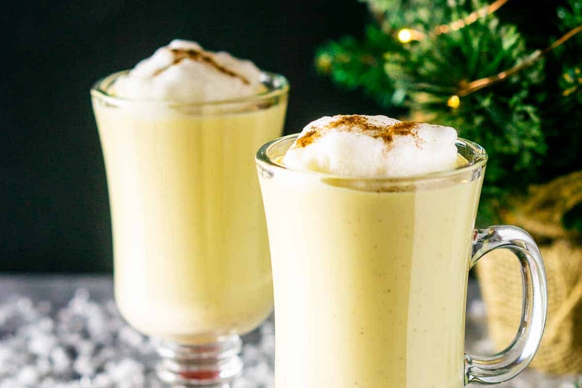 Two cups of hot cocoa with cinnamon whipped cream and a Christmas tree.