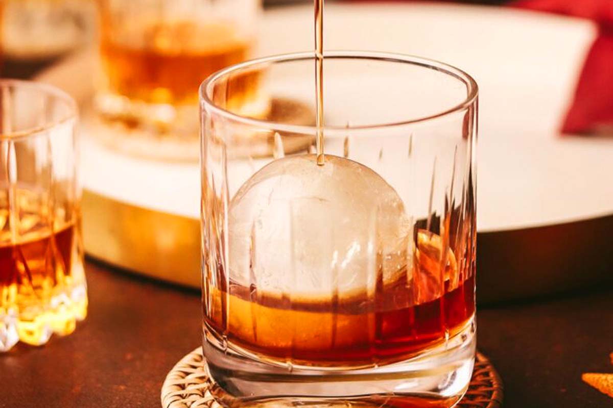 A glass of whiskey with an ice ball in it, perfect for enjoying authentic Canadian recipes.