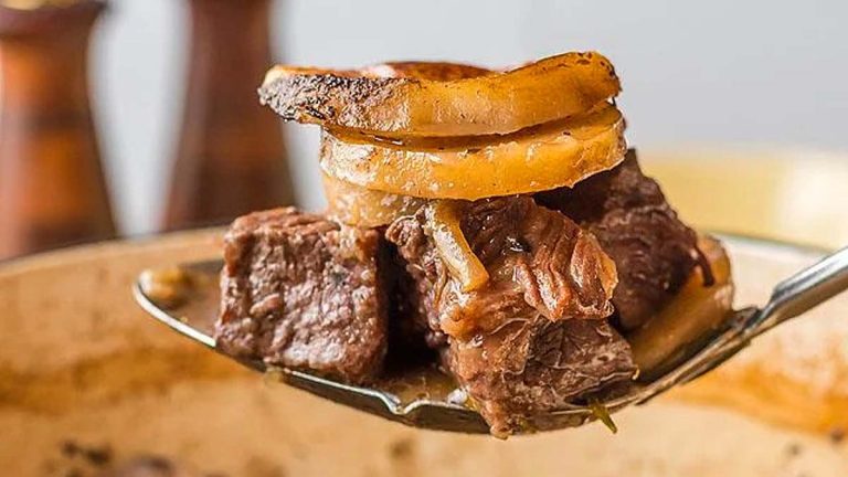 A spoon full of beef and onions in gravy.