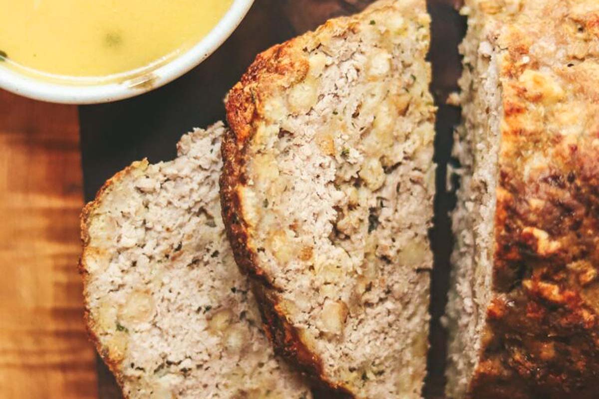 A loaf of bread with a dipping sauce on a cutting board, perfect for meatloaf recipes.