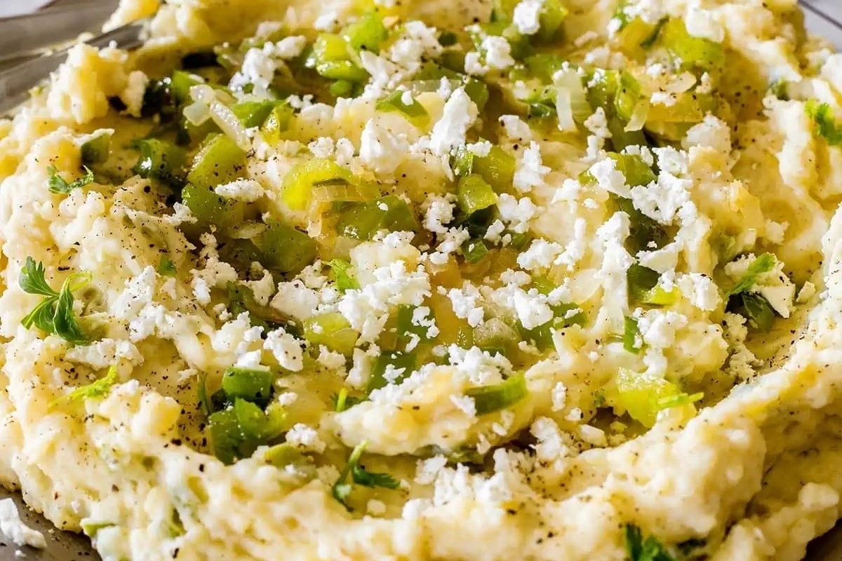 A bowl of mashed potatoes with green onions and feta cheese.